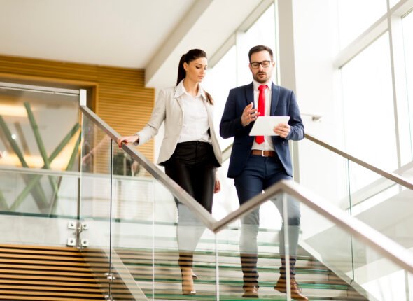 Young businesswoman and businessman walk down stairs in office with a tablet in his hand